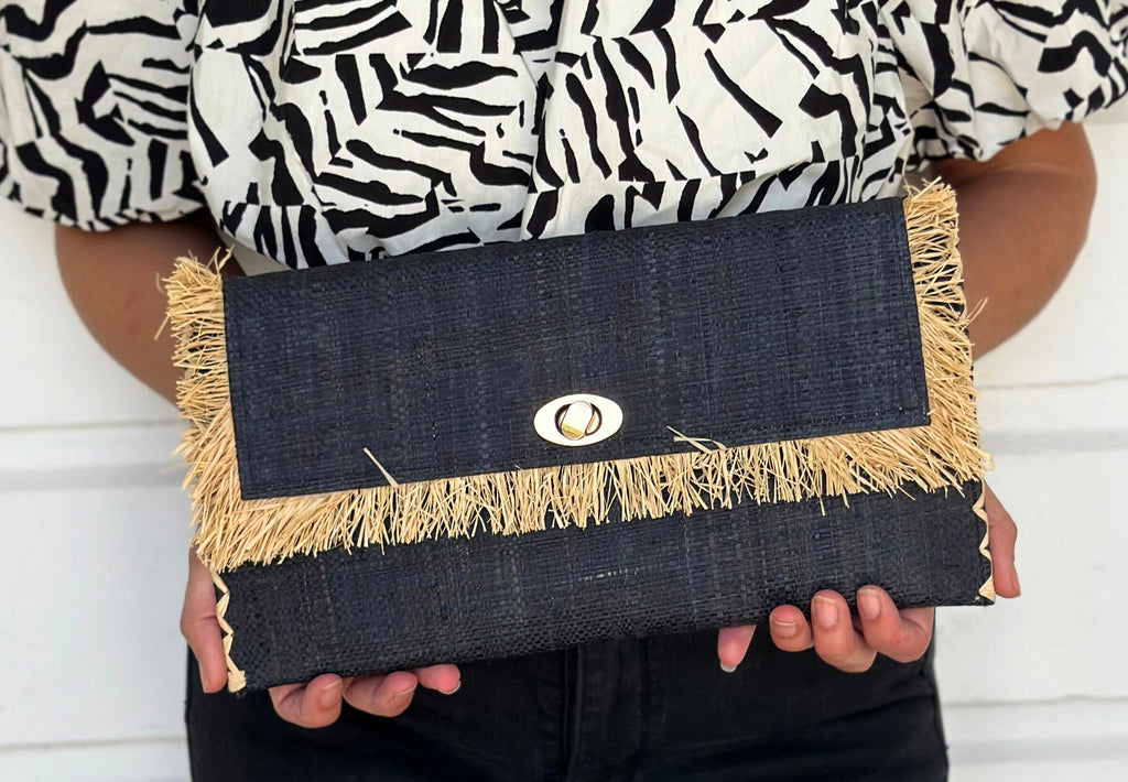 Model wearing Sophie Black Straw Clutch with Raw Fringe Edge handmade loomed black raffia purse with contrasting natural straw color fringe trim edge and matching cross stitch binding handbag - Shebobo