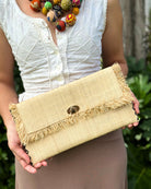 Model wearing Sophie Natural Straw Clutch with Raw Fringe Edge handmade loomed natural straw color raffia purse with matching fringe trim edge and contrasting black cross stitch binding handbag - Shebobo