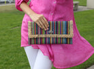 Model wearing Sophie Turquoise Stripes Multicolor Straw Clutch handmade loomed raffia purse handbag with raw fringe edge detailing turquoise, blue, natural, black, red, yellow, purple, orange, green, fuchsia, etc. multi width multicolor vertical stripe pattern envelope shaped bag - Shebobo