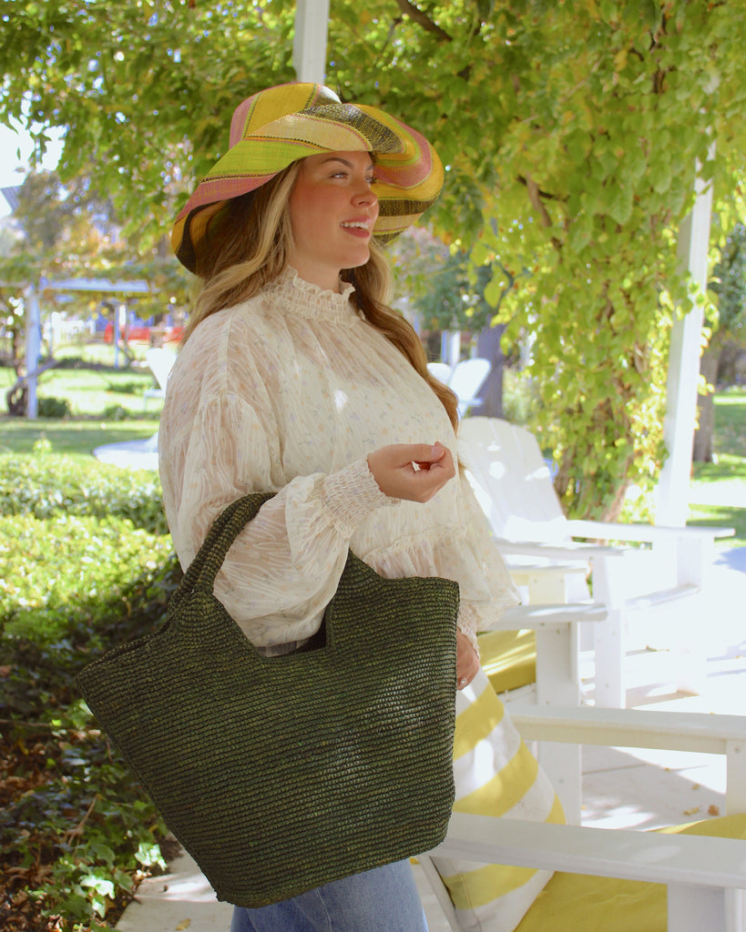 Model wearing St. Tropez Heart Shaped Crochet Straw Basket Handbag handmade crochet natural raffia palm fiber in a solid hue of Deep Green dark/forrest/green with a subtle link texture beach bag shoulder bag - Shebobo (with Monica 5" & 7" Wide Brim Multicolor Stripe Pattern Packable Straw Sun Hats)