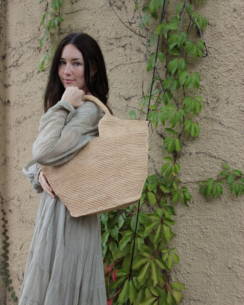 Model wearing St. Tropez Heart Shaped Crochet Straw Basket Handbag handmade crochet natural raffia palm fiber in a solid hue of natural straw color with a subtle link texture beach bag shoulder bag - Shebobo