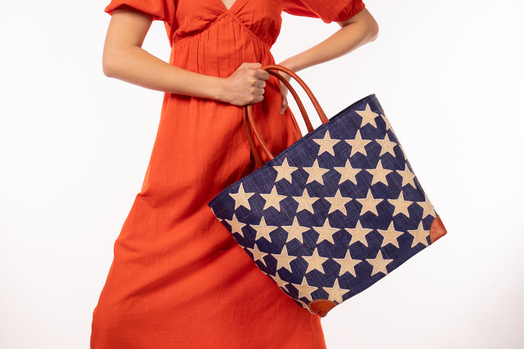 Model wearing Stars Straw Basket Bag handmade loomed raffia palm fiber in a solid hue of Dusk navy/dark/blue with natural straw color loomed stars stitched on in a tight  diagonal pattern with leather handles Patriotic Americana Shoulder Bag Beach Bag - Shebobo