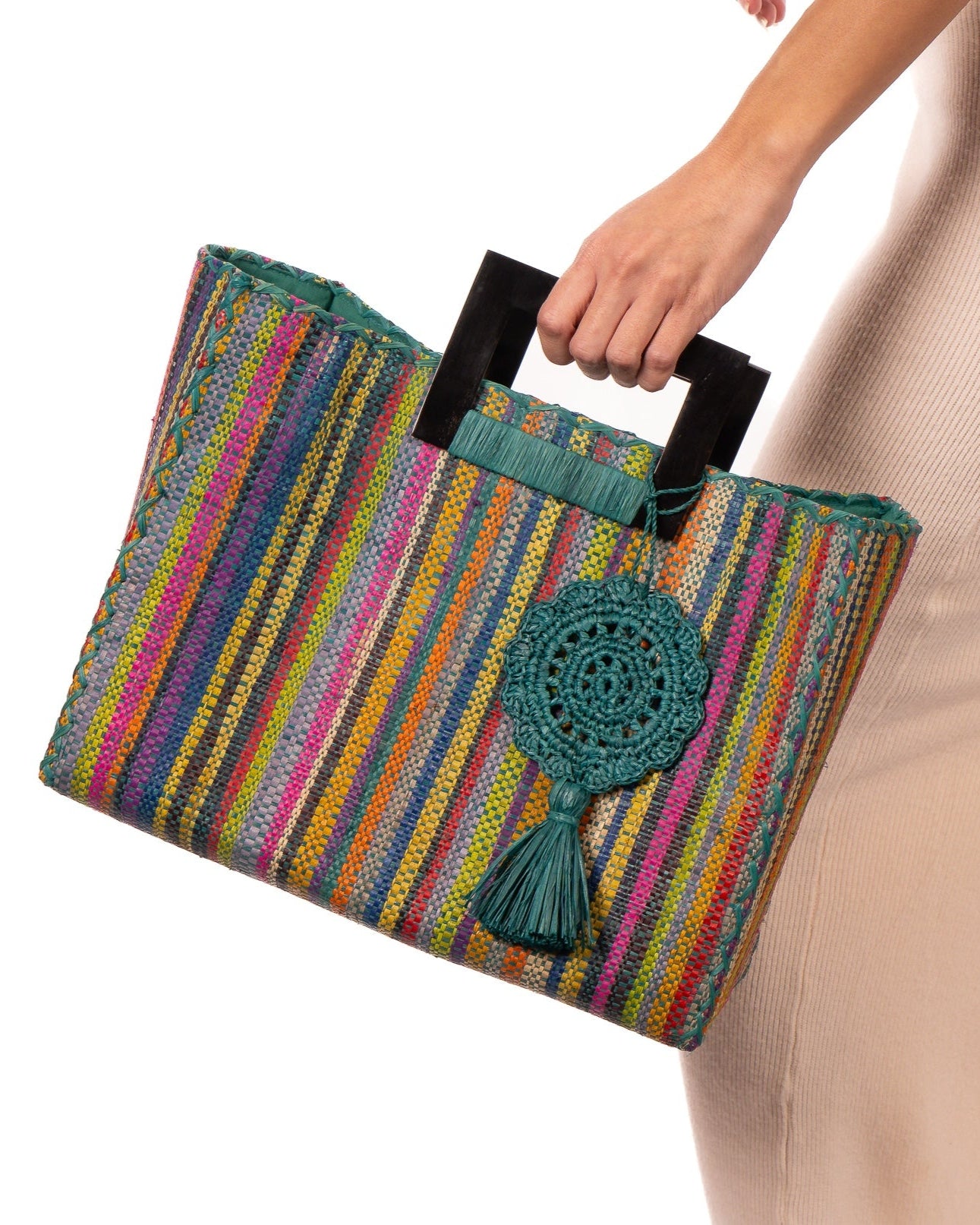 Model wearing Stevie Square Turquoise Stripes Multicolor Straw Handbag with Horn Handles handmade loomed raffia with turquoise, navy, light blue, purple, red, black, fuchsia, orange, yellow, lime, etc. varying width vertical stripe pattern purse with matching turquoise liner, cross stitch edging, handle attachment, and crochet doily tassel embellishment - Shebobo