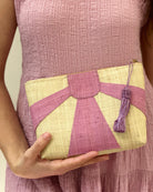 Model wearing Sunburst Cosmetic Clutch with Tassel Zipper Pull handmade zippered pouch purse with sunburst pattern of wisteria/lavender/lilac pink/purple on natural loomed raffia palm fibers and matching colored tassel pull handbag - Shebobo
