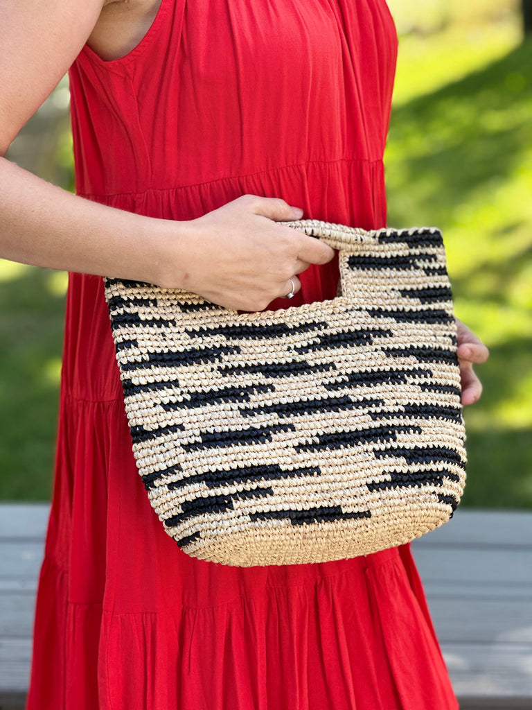 Model wearing Taylor Mini ConCon Crochet Natural Straw Basket with Zebra Stripes handmade raffia palm fiber in a horizontal zebra stripe with short lengths of contrasting color in a dash pattern of natural straw color with black accent petite handbag purse - Shebobo