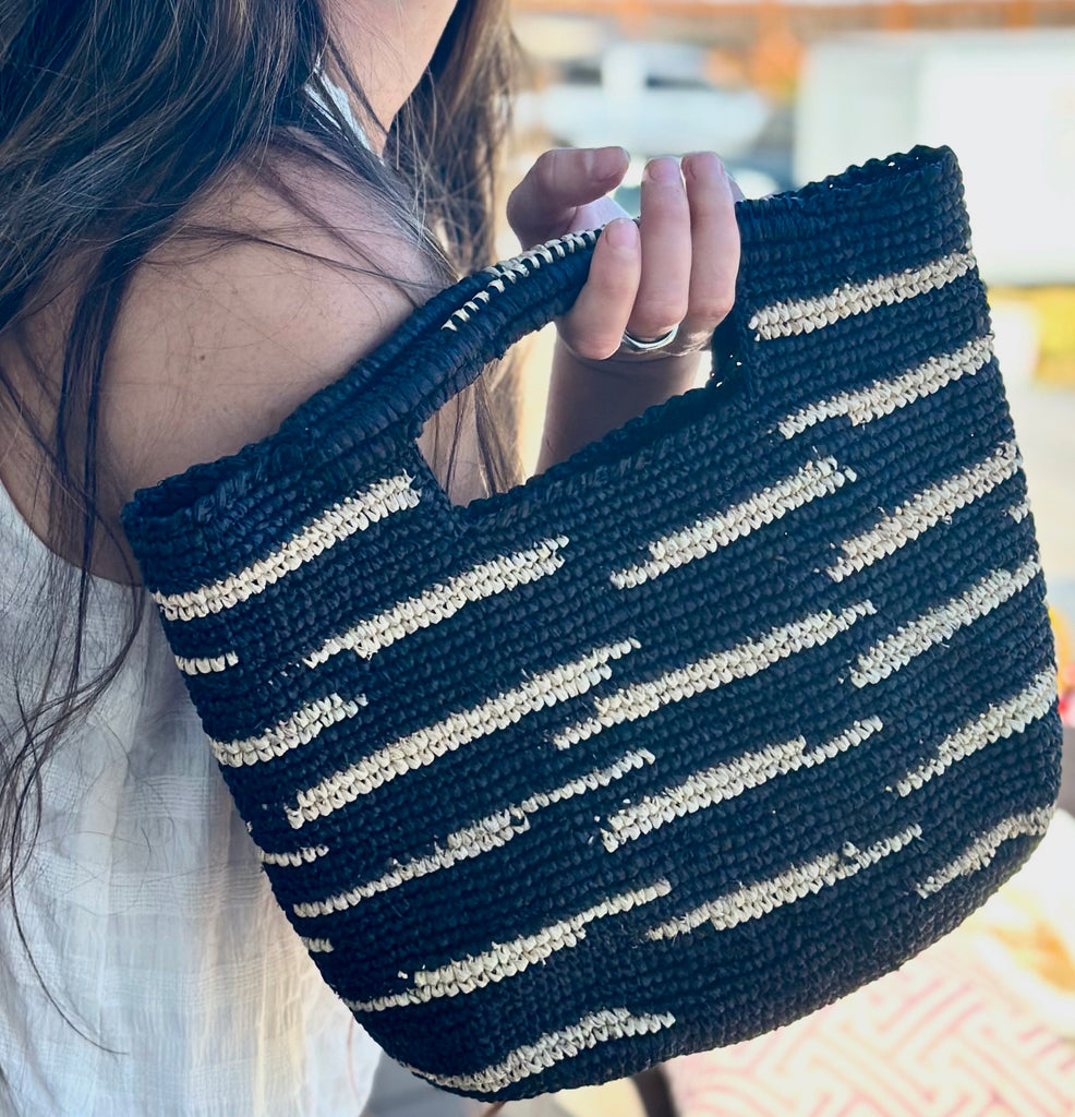 Model wearing Taylor Mini ConCon Crochet Black Straw Basket with Zebra Stripes handmade raffia palm fiber in a horizontal zebra stripe with short lengths of contrasting color in a dash pattern of black with natural straw color accent petite handbag purse - Shebobo