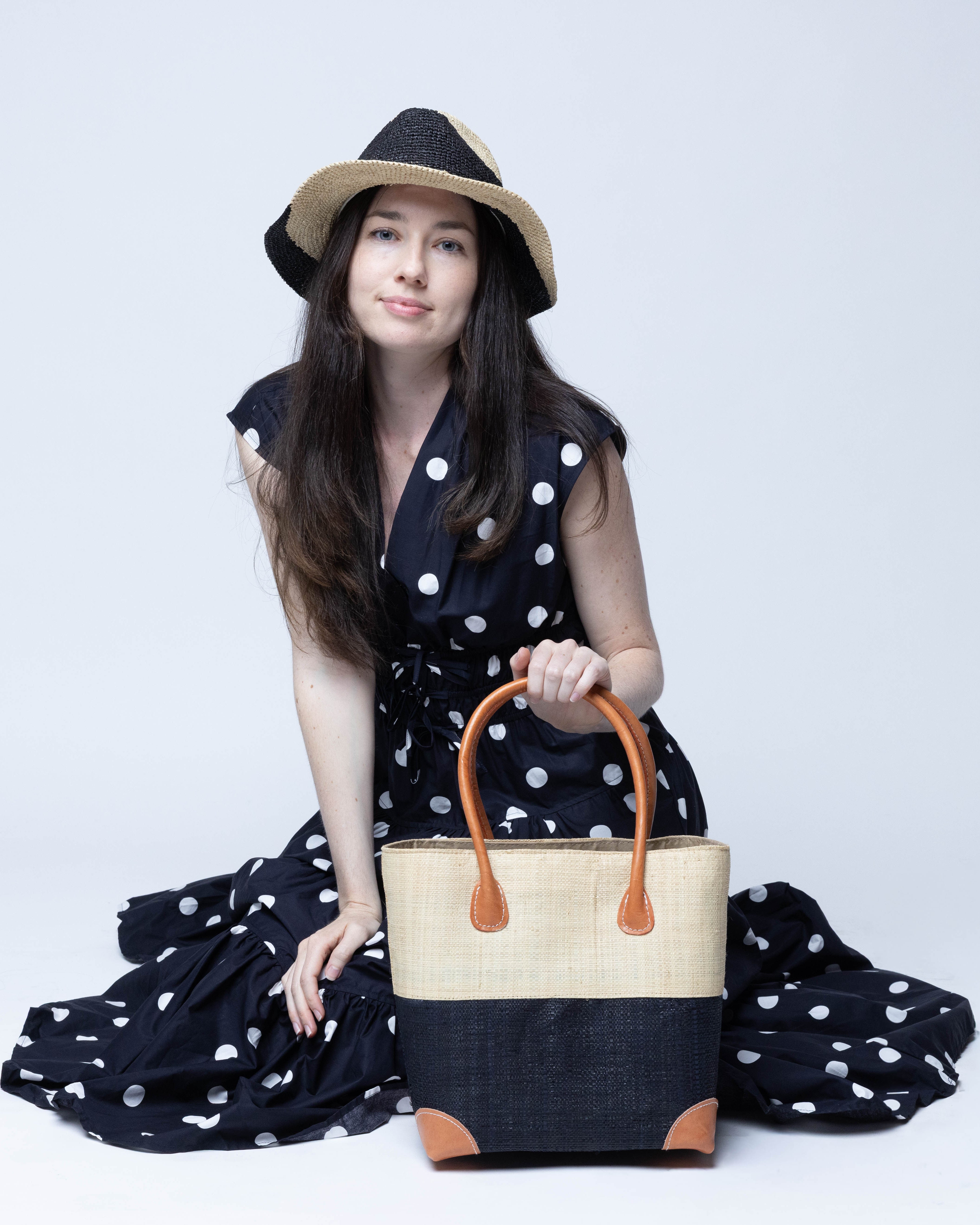 Model wearing Trinidad Natural and Black Two Tone Straw Basket Bag handmade loomed raffia palm fiber in a two tone color block pattern with black on the bottom half and natural straw color on the top half of the bag with leather handles and accents beach bag tote purse - Shebobo (with Sequoia 3" Brim Swirl Crochet Panama Unisex Straw Hats)