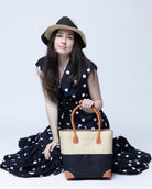 Model wearing Trinidad Natural and Black Two Tone Straw Basket Bag handmade loomed raffia palm fiber in a two tone color block pattern with black on the bottom half and natural straw color on the top half of the bag with leather handles and accents beach bag tote purse - Shebobo (with Sequoia 3" Brim Swirl Crochet Panama Unisex Straw Hats)