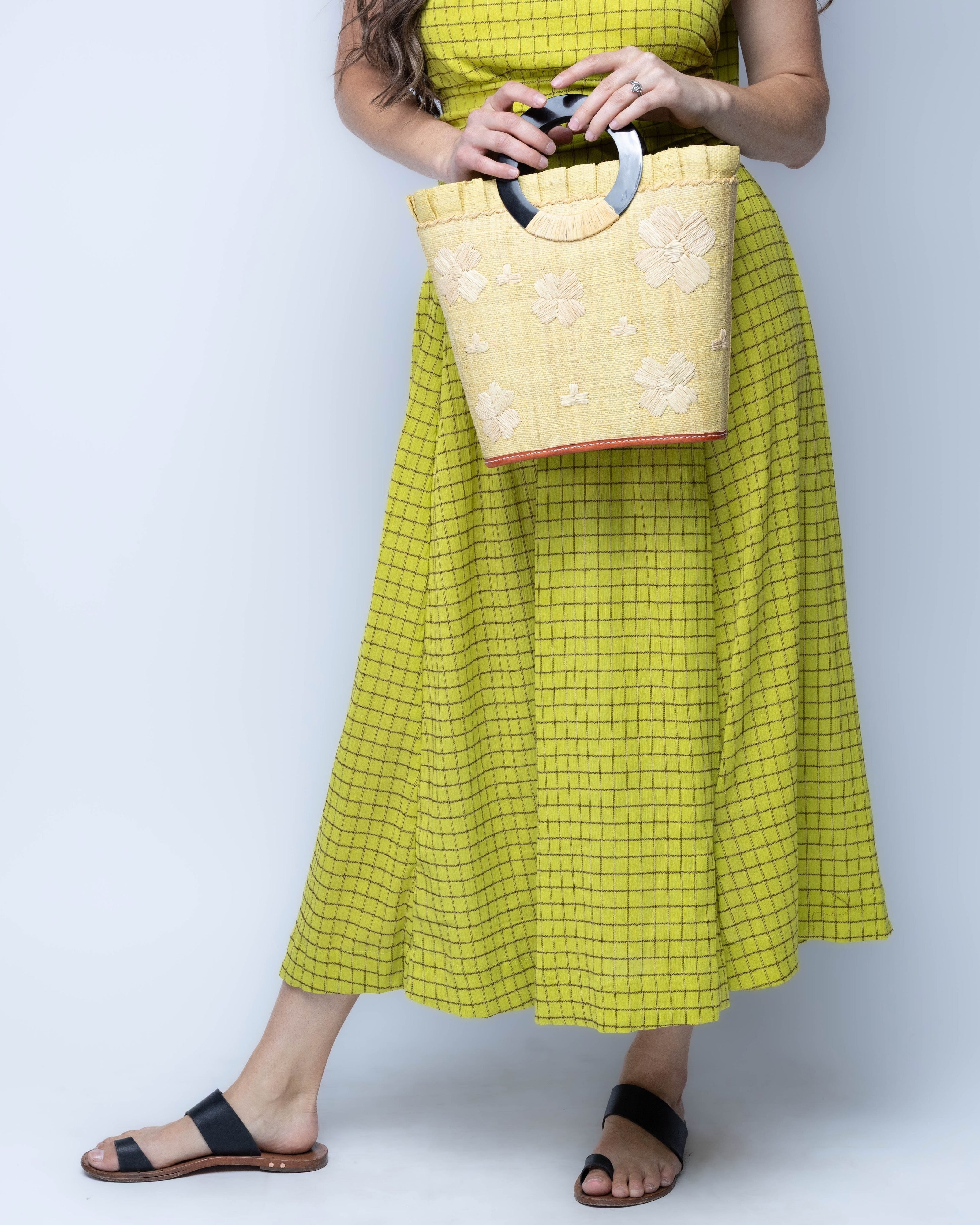 Model wearing Tulum Straw Bucket Bag with Flower Embroidery and Horn Handle Butter Purse with Ruffle Edge handmade loomed raffia palm fiber in a solid hue of butter light/yellow with natural straw color hand embroidered floral pattern with multiple sized flowers and raffia ruffle on the opening  handbag - Shebobo