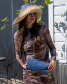 Model wearing Tulum Clutch Denim retro/light/blue Flower Embroidery handmade loomed raffia palm fibers with envelope clutch shape, embroidered multi-sized embroidered flower pattern, and assorted interior wax cloth African Print liners plus zippered pocket  - Shebobo (with 7" Wide Brim Denim and Natural Two Tone Packable Straw Sun Hats)