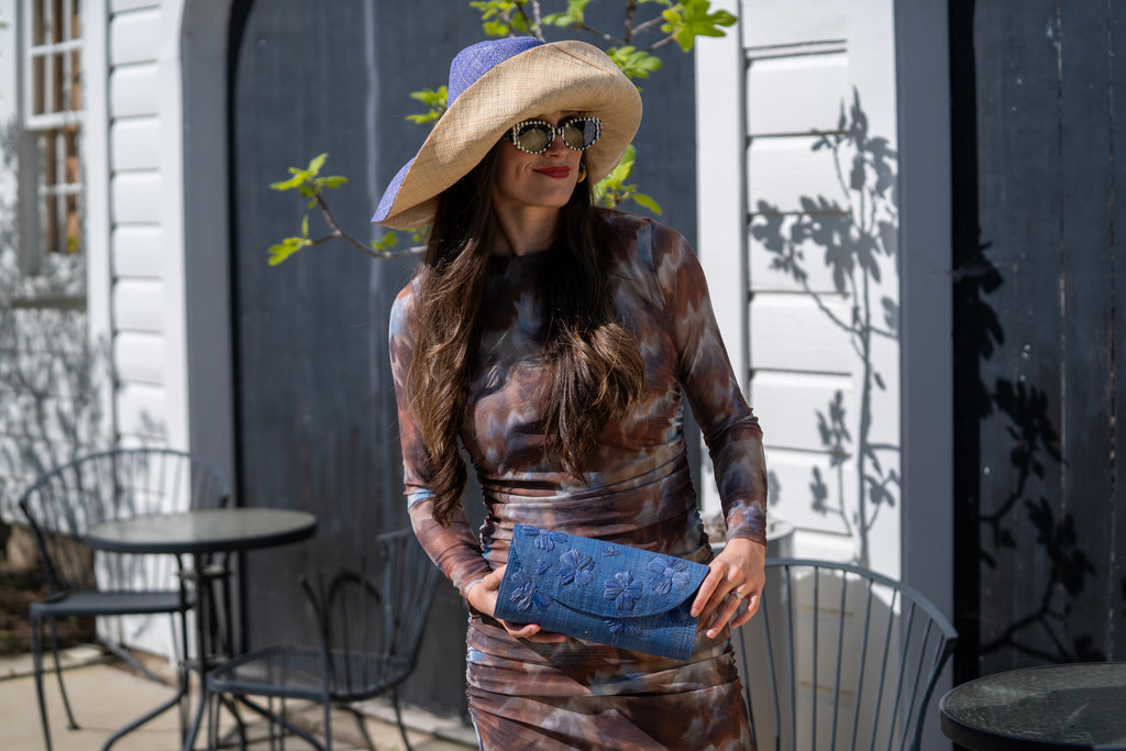 Model wearing Tulum Clutch Denim retro/light/blue Flower Embroidery handmade loomed raffia palm fibers with envelope clutch shape, embroidered multi-sized embroidered flower pattern, and assorted interior wax cloth African Print liners plus zippered pocket  - Shebobo (with 7" Wide Brim Denim and Natural Two Tone Packable Straw Sun Hats)