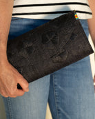 Model wearing Tulum Clutch Black Flower Embroidery handmade loomed raffia palm fibers with envelope clutch shape, embroidered multi-sized embroidered flower pattern, and assorted interior wax cloth African Print liners plus zippered pocket  - Shebobo