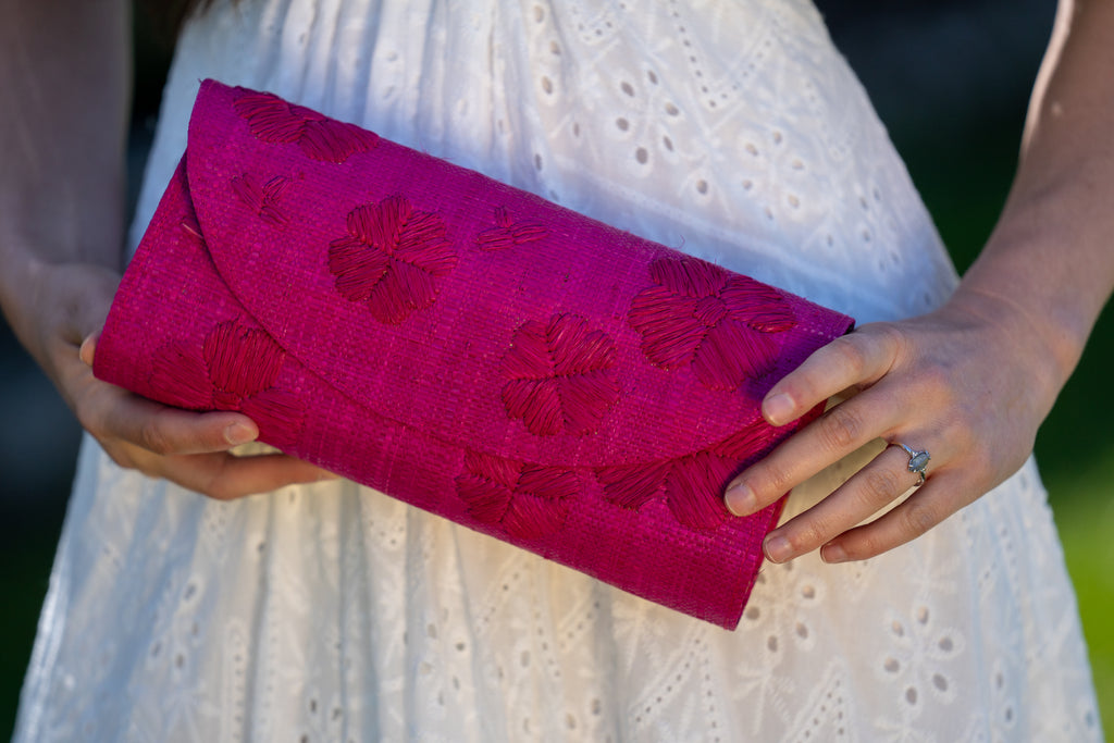 Model wearing Tulum Clutch Fuchsia hot/bright/barbie/pink Flower Embroidery handmade loomed raffia palm fibers with envelope clutch shape, embroidered multi-sized embroidered flower pattern, and assorted interior wax cloth African Print liners plus zippered pocket  - Shebobo