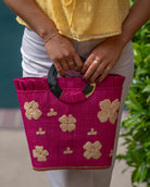 Model wearing Tulum Straw Bucket Bag with Flower Embroidery and Horn Handle Fuchsia Purse with Ruffle Edge handmade loomed raffia palm fiber in a solid hue of fuchsia hot/bright/barbie/pink with natural straw color hand embroidered floral pattern with multiple sized flowers and raffia ruffle on the opening  handbag - Shebobo