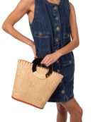 Model wearing Tulum Straw Bucket Bag with Flower Embroidery and Horn Handle Natural Purse with Ruffle Edge handmade loomed raffia palm fiber in a solid hue of natural straw color with matching subtle hand embroidered floral pattern with multiple sized flowers and raffia ruffle on the opening  handbag - Shebobo