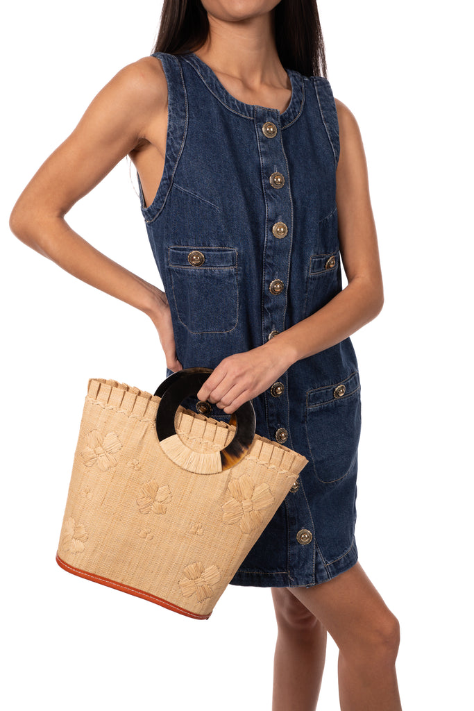 Model wearing Tulum Straw Bucket Bag with Flower Embroidery and Horn Handle Natural Purse with Ruffle Edge handmade loomed raffia palm fiber in a solid hue of natural straw color with matching subtle hand embroidered floral pattern with multiple sized flowers and raffia ruffle on the opening  handbag - Shebobo