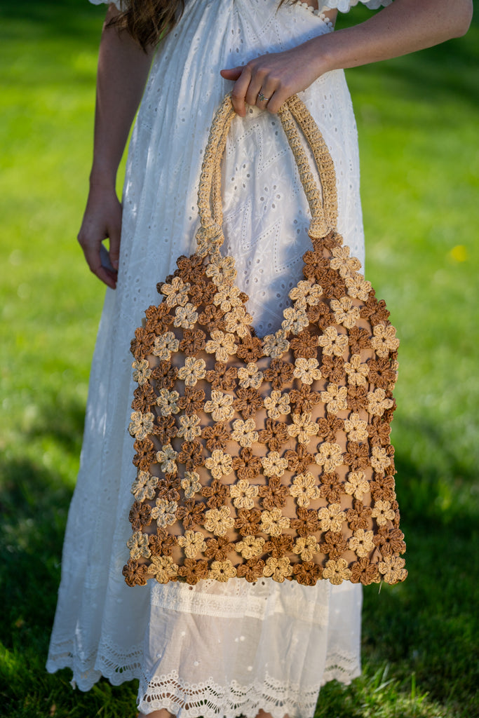 Model wearing Two Tone Daisy Flower Crochet Straw Handbag handmade crochet mini flower buds from crochet natural raffia palm fiber in an alternating colored pattern of cappuccino tea/light/brown and natural straw color with brown internal liner and natural woven handles purse - Shebobo