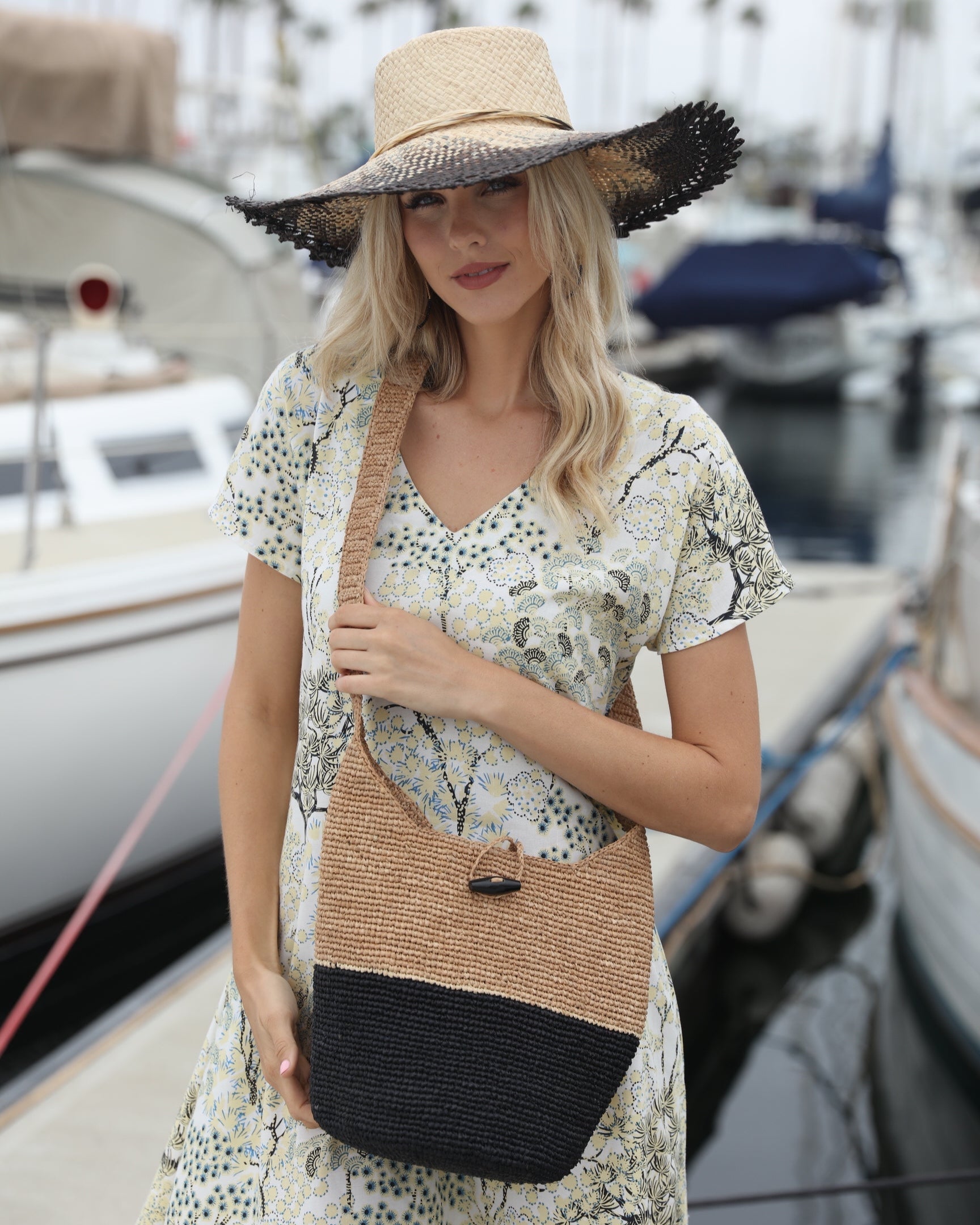 Model wearing CoronadoTwo Tone Crochet Crossbody Bag handmade with interior liner, horn button and loop closure raffia purse black bottom, with narrow natural straw color horizontal stripe separating light brown/tea colored top & shoulder strap - Shebobo *dress by Kikisol