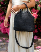 Model wearing Victoria Crochet Straw Handbag Convertible Crossbody Bag handmade crochet natural raffia palm fiber in a solid hue of black in a subtle texture of horizontal link bands pattern across the bag and m shape around the top of the bag with black leather handles and removable matching crossbody strap convertible purse - Shebobo
