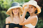 Models wearing Monica 5" wide brim packable two tone handmade loomed raffia fiber black and natural straw hat along with Monica 5" wide brim pinstripe pattern natural with black stripe packable straw sun hat - Shebobo
