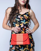 Model wearing Wynwood Coral Straw Handbag with Metallic Detailing & Horn Handle handmade loomed raffia in coral orange/red and metallic vegan leather in three vertical bands of color with the metallic weave centered on the purse under the handles - Shebobo