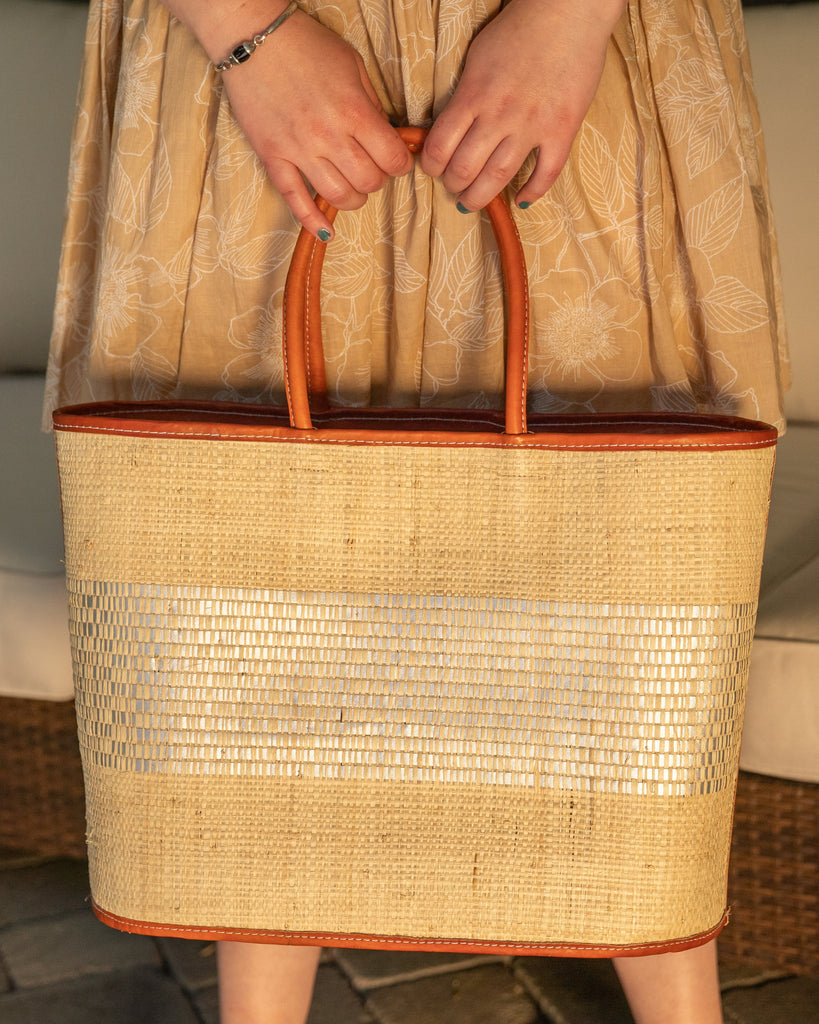 Model wearing Wynwood Natural Straw Basket Bag Handbag with Metallic Detailing handmade loomed raffia in natural straw color and silver metallic vegan leather in three evenly sized horizontal bands of color with the metallic weave centered on the purse with leather binding and handles - Shebobo