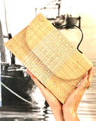 Model holding Wynwood Natural Straw Handbag with Metallic Detailing & Horn Handle handmade loomed raffia in natural straw color and silver metallic vegan leather in three vertical bands of color with the metallic weave centered on the purse under the handles - Shebobo