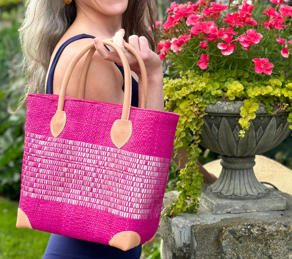 Model wearing Wynwood Fuchsia Straw Basket Bag with Metallic Detailing Handmade loomed raffia palm fiber in a solid hue of fuchsia bright/hot/barbie/pink with a wide horizontal band of metallic strands woven in seamlessly handbag purse with leather handles - Shebobo
