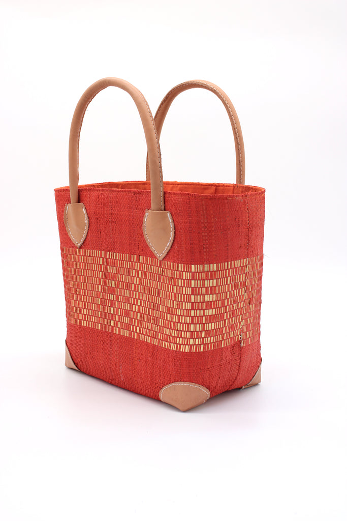 Side View Wynwood Coral Straw Basket Bag with Metallic Detailing Handmade loomed raffia palm fiber in a solid hue of coral orange/red with a wide horizontal band of metallic strands woven in seamlessly handbag purse with leather handles - Shebobo