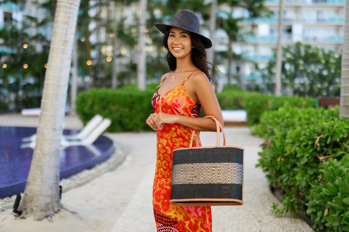 Model wearing Wynwood Black Straw Basket Bag Handbag with Metallic Detailing handmade loomed raffia in black and silver metallic vegan leather in three evenly sized horizontal bands of color with the metallic weave centered on the purse with leather binding and handles - Shebobo (with Jamie 3" Brim Panama Unisex Raffia Straw Hats)