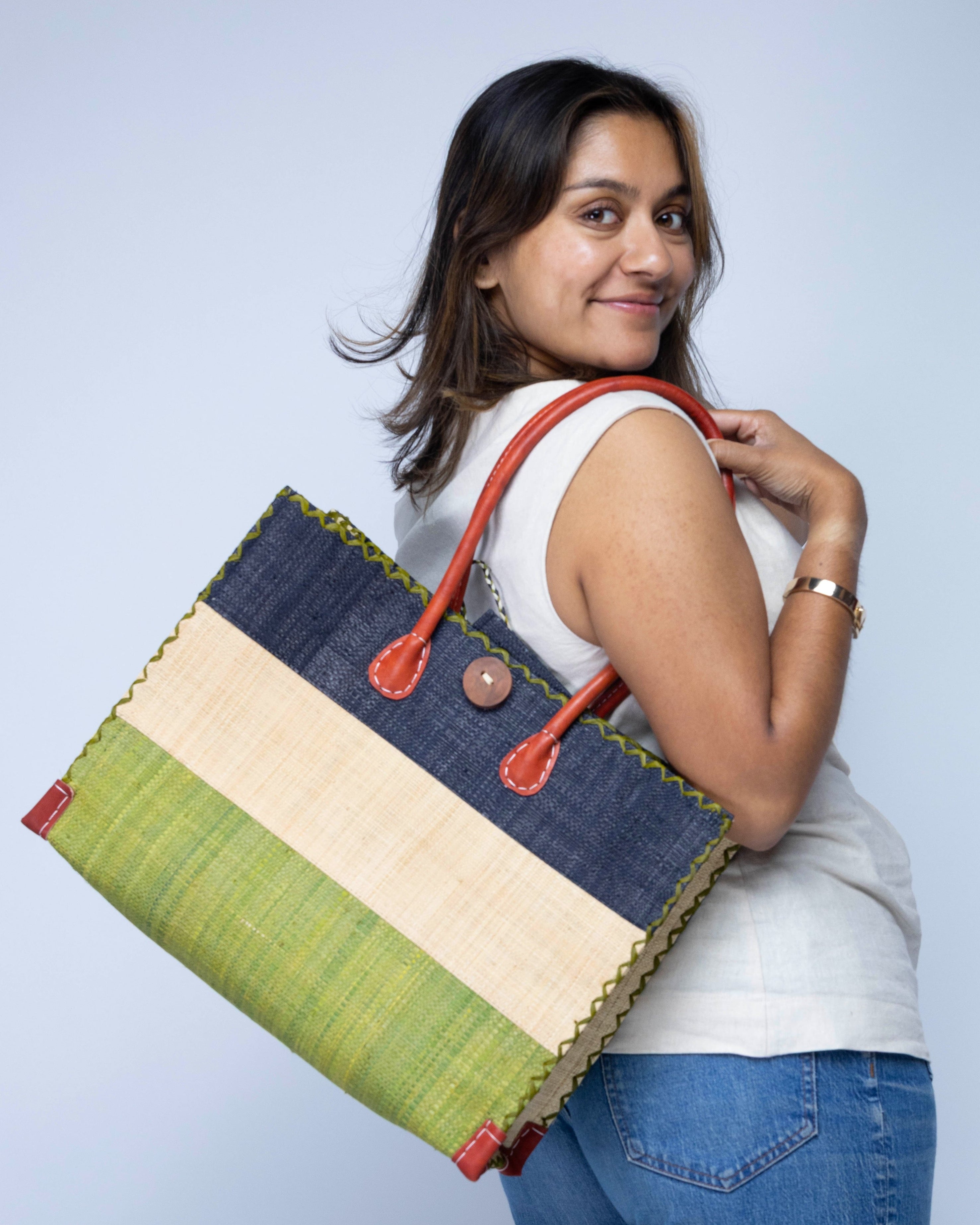 Model wearing Small Zafran 3 Tone Color Block Beach Straw Bag with Plastic Liner handmade loomed raffia palm fiber in three equally sized horizontal bands of black, natural straw color, and martini olive/dark/green with wood button and leather handles - Shebobo