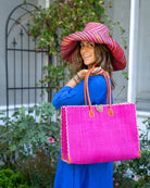 Zafran Straw Beach Bag with Plastic Liner handmade loomed raffia in a solid hue of Fuchsia hot/bright/barbie/pink with contrasting natural straw color cross stitch edge binding, wood button closure, and leather handles & feet plus assorted print plastic lining - Shebobo (with Monica 5" & 7" Wide Brim Very Berry Multicolor Melange Pattern Packable Straw Sun Hats)