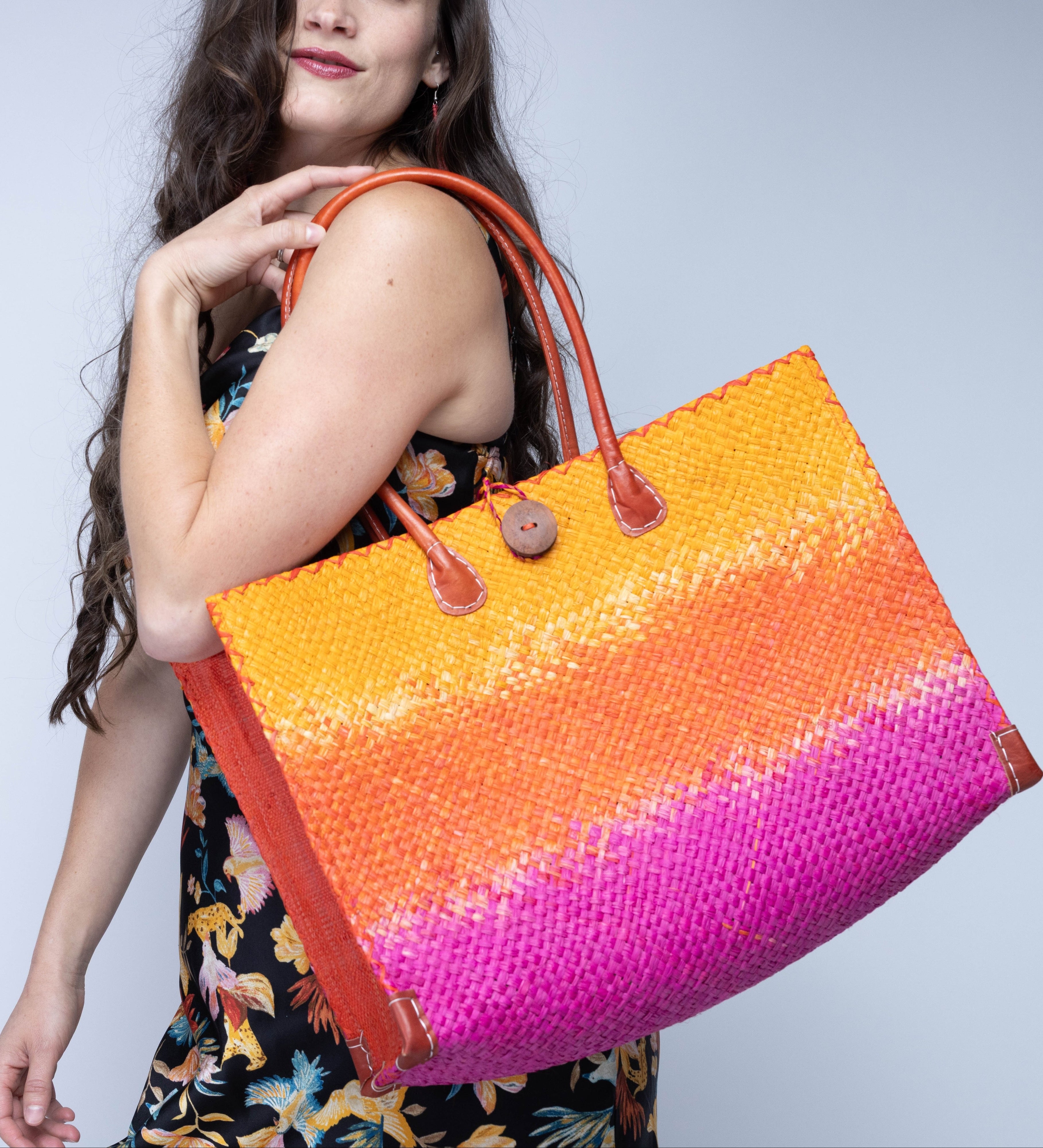 Model wearing Small Holden Fuchsia Ombre Zafran Straw Beach Bags handmade dip dyed raffia woven into a three part horizontal ombre pattern of coral orange/red, fuchsia pink, and saffron yellow with cross stitch edging, wooden button, and leather handles - Shebobo
