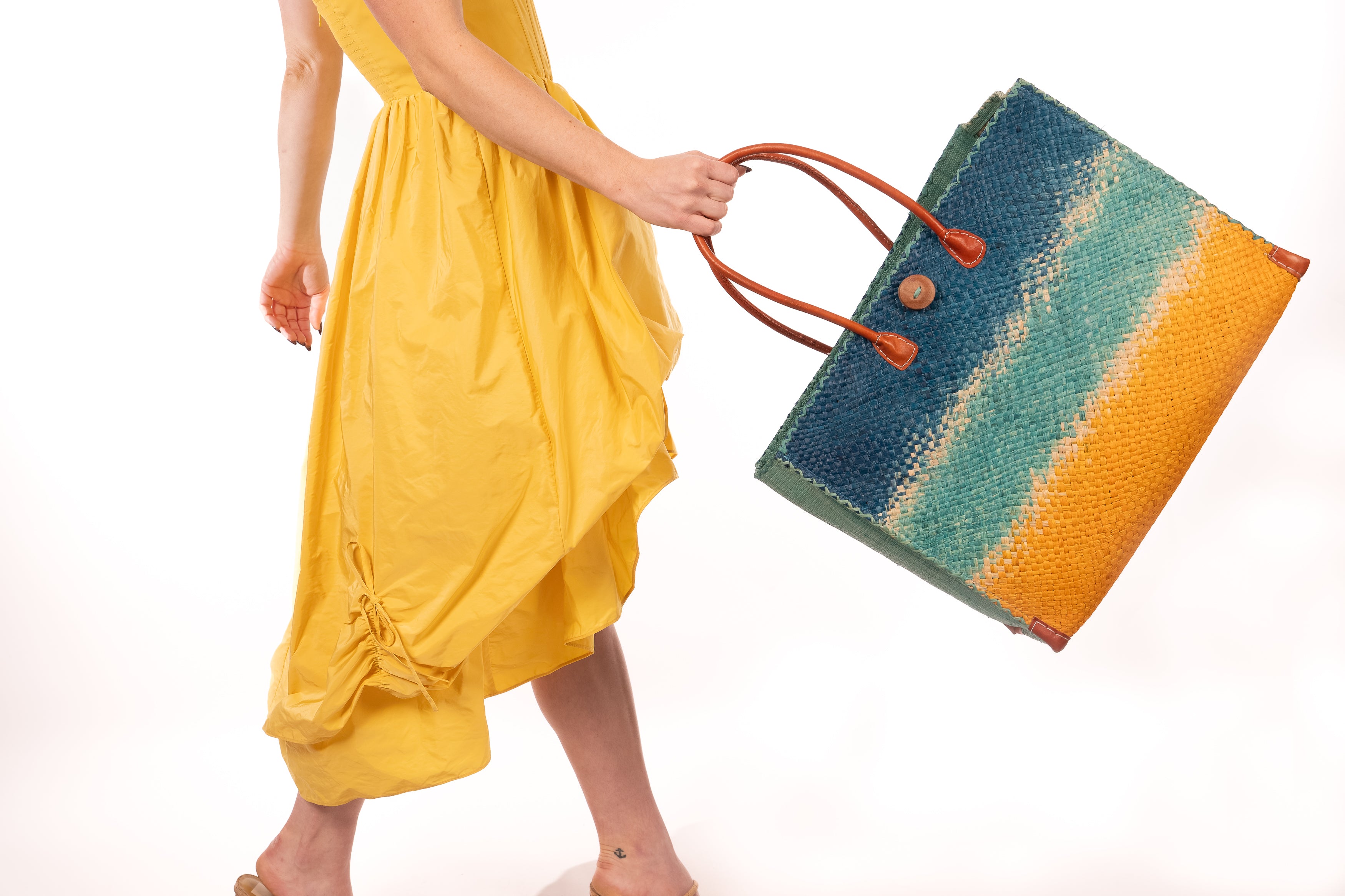 Model wearing Model wearing Holden Turquoise Ombre Zafran Large Straw Beach Bags handmade dip dyed raffia woven into a three part horizontal ombre pattern of turquoise blue on the top, seafoam blue/green in the middle and both sides, and saffron yellow on the bottom with cross stitch edging, wooden button, and leather handles - Shebobo