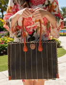 Model wearing Zafran Black Pinstripes Large Straw Beach Bag with Plastic Liner handmade loomed raffia tote in wide bands of black with narrow bands of natural straw color that make a vertical pinstripe pattern with assorted print plastic lining and leather handles bag - Shebobo
