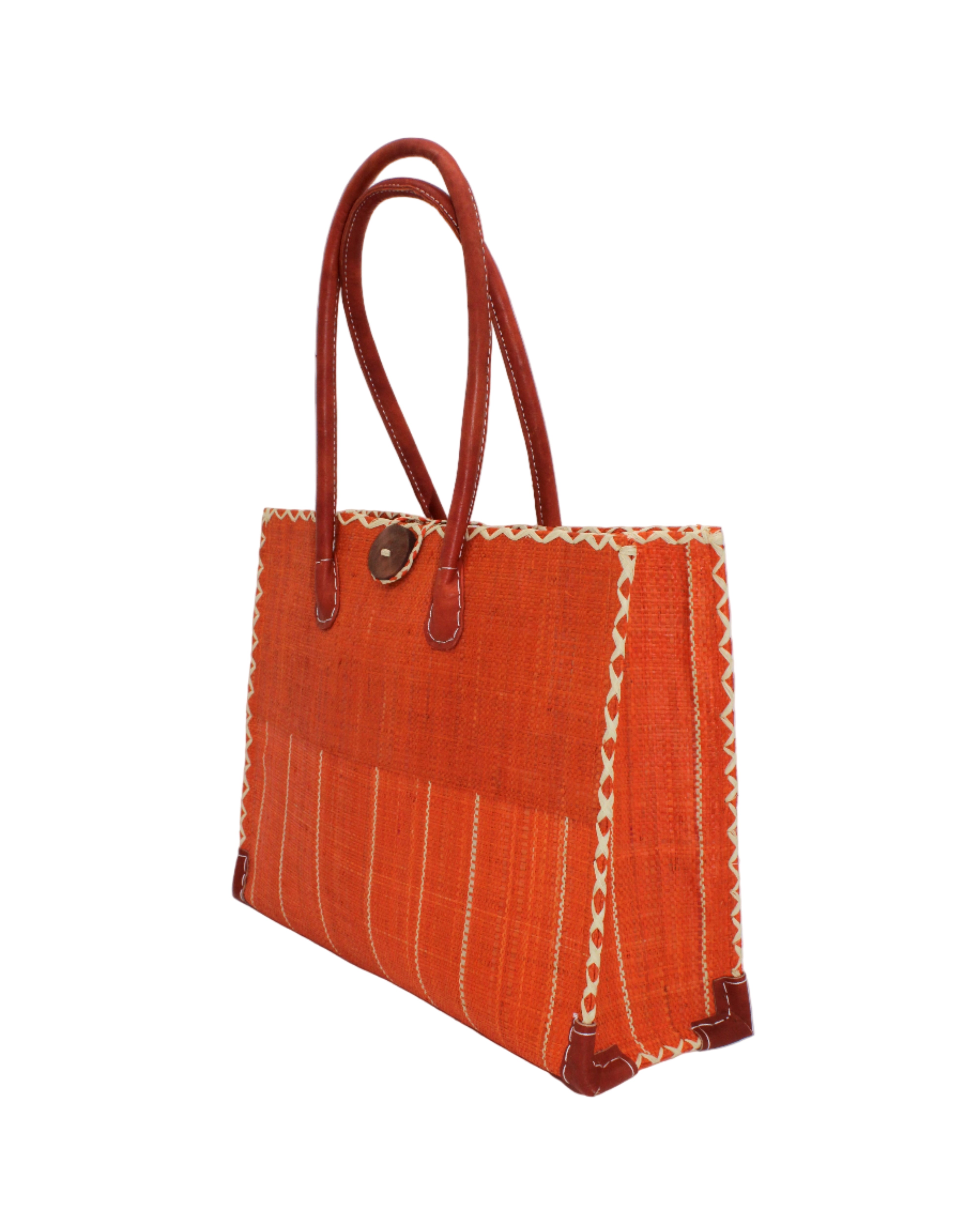 Side view Zafran Two Tone Wide Stripe Coral Pinstripe Straw Beach Bag handmade loomed raffia palm fiber in a solid hue of coral orange/red on the top half of the bag and a multicolor multi-width vertical pinstripe stripe pattern with thin bands of natural straw color with wide bands of coral on the bottom half of the bag with leather handles and feet and matching crosshatch stitch edging shoulder bag - Shebobo