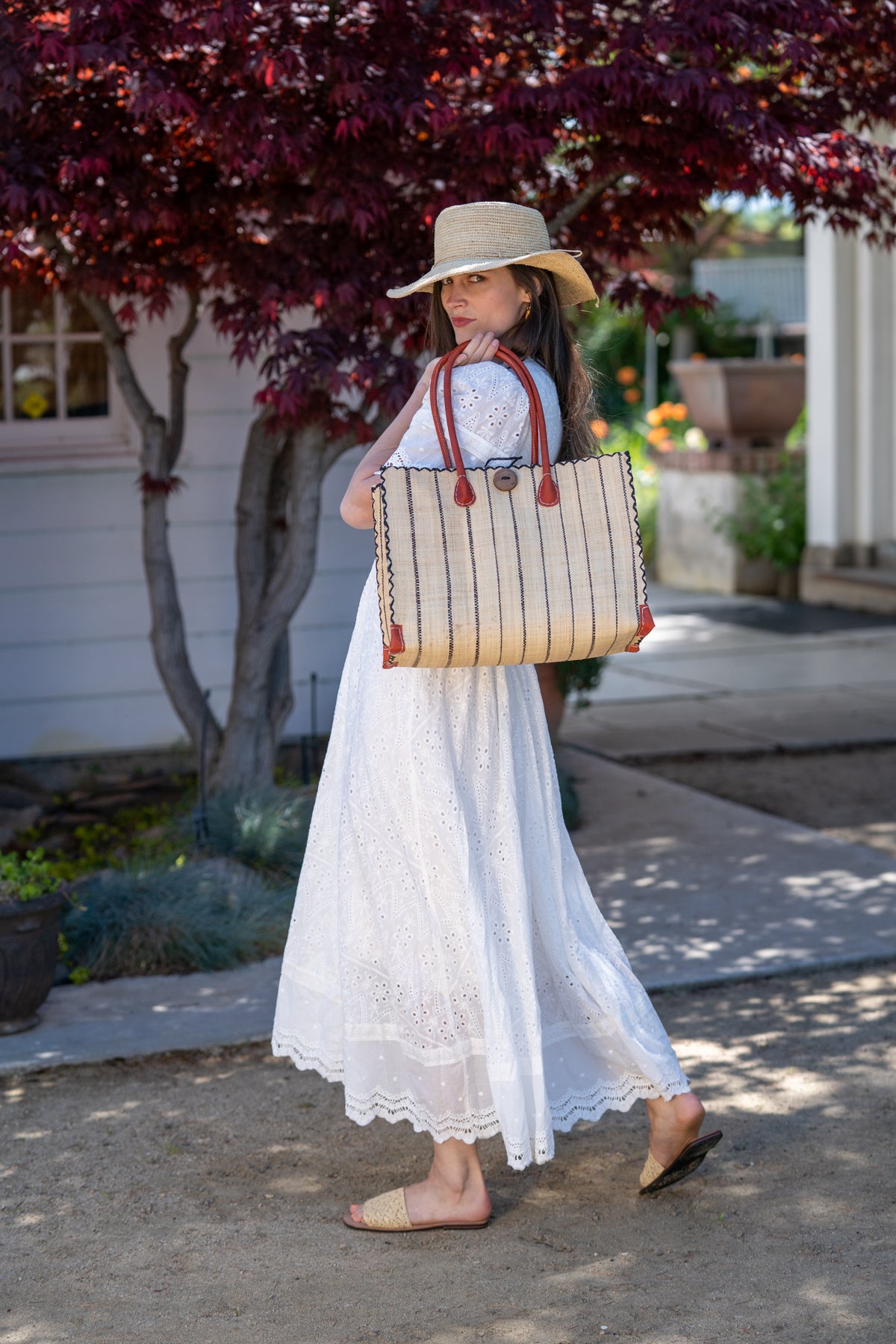Model wearing Small Zafran Natural Pinstripes Large Straw Beach Bag with Plastic Liner handmade loomed raffia tote in wide bands of natural straw color with narrow bands of black that make a vertical pinstripe pattern with assorted print plastic lining and leather handles xl bag - Shebobo (with Bolero Natural Crochet Straw Sun Hat and Lulu Natural Macrame Straw Sandal)
