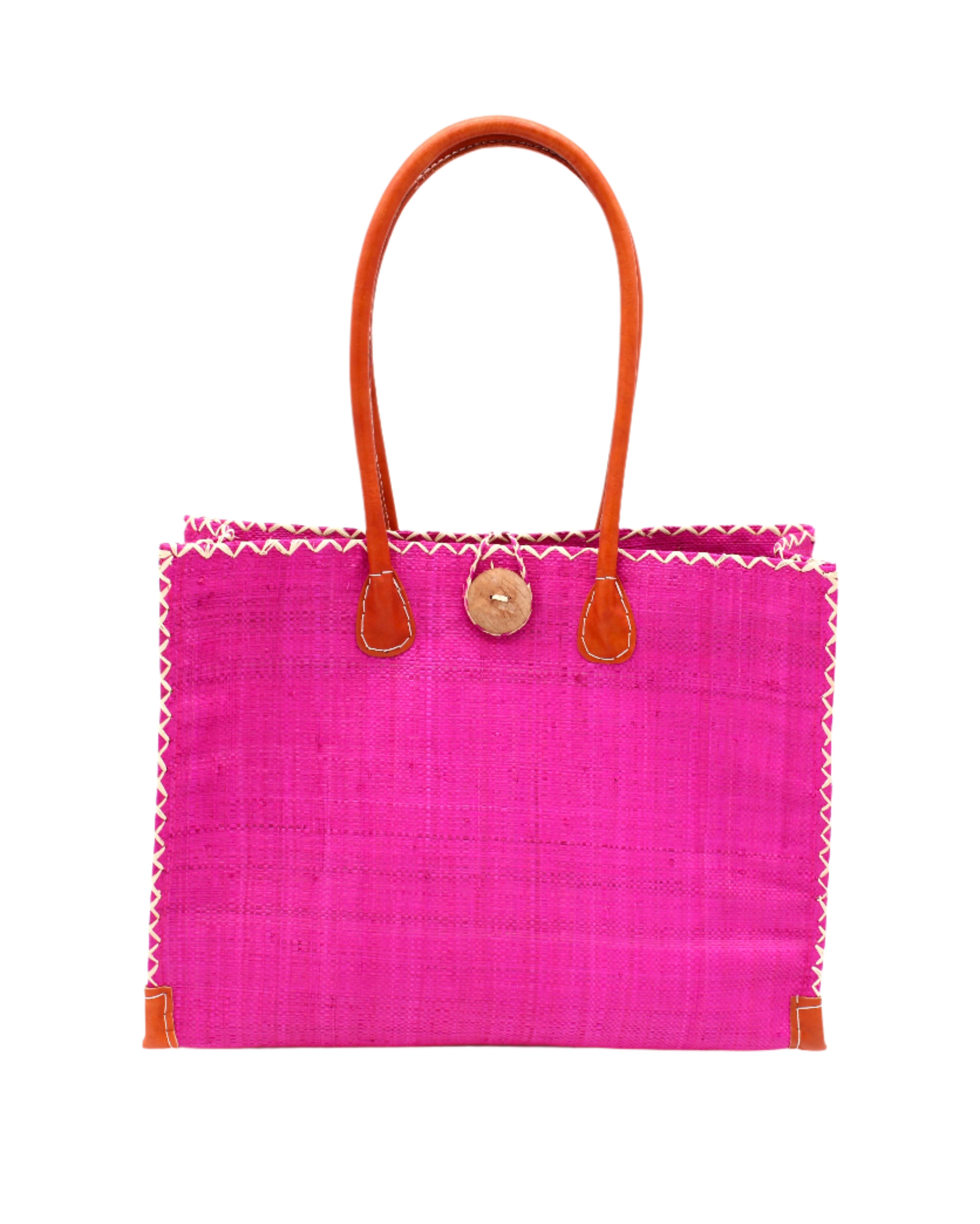 Zafran Straw Beach Bag with Plastic Liner handmade loomed raffia in a solid hue of Fuchsia hot/bright/barbie/pink with contrasting natural straw color cross stitch edge binding, wood button closure, and leather handles & feet plus assorted print plastic lining - Shebobo