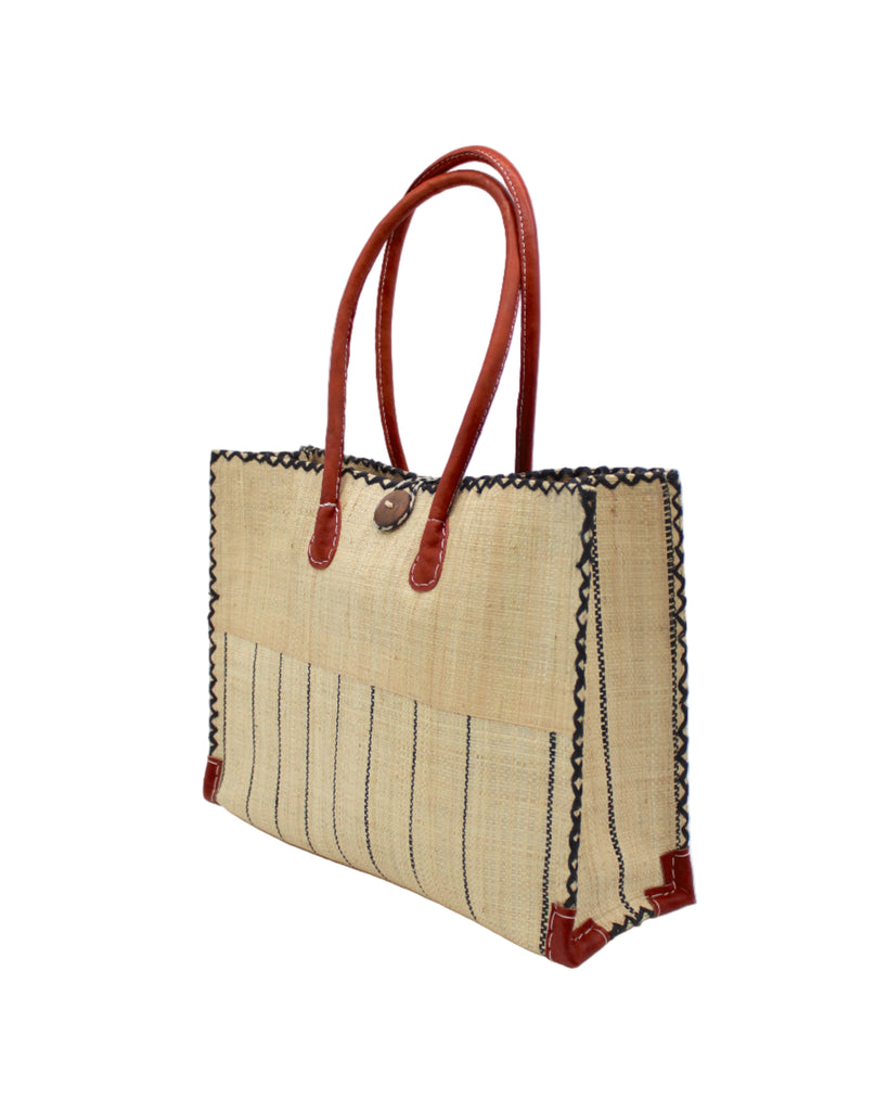 Side view Zafran Two Tone Wide Stripe Natural Pinstripe Straw Beach Bag handmade loomed raffia palm fiber in a solid hue of natural straw color on the top half of the bag and a multicolor multi-width vertical pinstripe stripe pattern with thin bands of black with wide bands of natural on the bottom half of the bag with leather handles and feet and matching crosshatch stitch edging shoulder bag - Shebobo