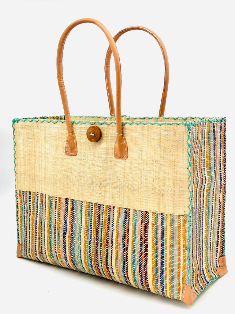 Side view Zafran Two Tone Taffy Multicolor Stripes Beach Straw Bag with Plastic Liner handmade loomed raffia color block with the top half solid natural straw color and the bottom half multi width vertical stripes of natural, seafoam, bordeaux, orange, saffron, blue, etc. - sides of bag are same stripe pattern - with wood button and leather handles & accents - Shebobo