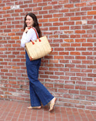Model wearing Zafran Two Tone Wide Stripe Neutrals Pinstripe Straw Beach Bag handmade loomed raffia palm fiber in a solid hue of natural straw color on the top half of the bag and a multicolor multi-width vertical pinstripe stripe pattern with thin bands of black, blush pink/orange, cinnamon tobacco/dark/brown, and grey with wide bands of natural straw color on the bottom half of the bag with leather handles and feet and matching crosshatch stitch edging shoulder bag - Shebobo