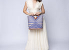 Model wearing Mariposa Zuki Raffia Straw Bucket Handbag with Wood Triangle Handles  handmade loomed raffia palm fiber in a multi paneled pattern design of pinstripe, melange, and wide stripe combinations geometrically radiating from the center point of the bag outwards in a two tone color combination of Denim and Natural straw color with a solid hue of color on the back of the bag plus carved wooden handles purse - Shebobo