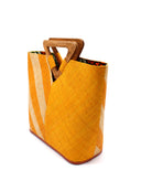 Side View Zuki Two Tone Saffron Straw Handbag With Wood Triangle Handle handmade loomed raffia palm fiber in a two tone pattern with the left half of the bag even width stripes of saffron yellow/orange and natural straw color oriented as a diagonal stripe and the right half of the bag a solid hue of saffron with carved wood handles - Shebobo