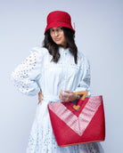 Model wearing Zuki Wynwood Red Straw Handbag with Metallic Detailing & Wood Triangle Handle handmade loomed raffia palm fiber in a solid hue of red with incorporated vegan leather  silver metallic strands in a V pattern across the front and back of the bag with assorted print African wax cloth liners and carved wooden triangle handle purse - Shebobo