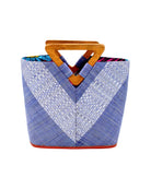 Zuki Wynwood Denim Straw Handbag with Metallic Detailing & Wood Triangle Handle handmade loomed raffia palm fiber in a solid hue of denim retro/light/blue with incorporated vegan leather  silver metallic strands in a V pattern across the front and back of the bag with assorted print African wax cloth liners and carved wooden triangle handle purse - Shebobo