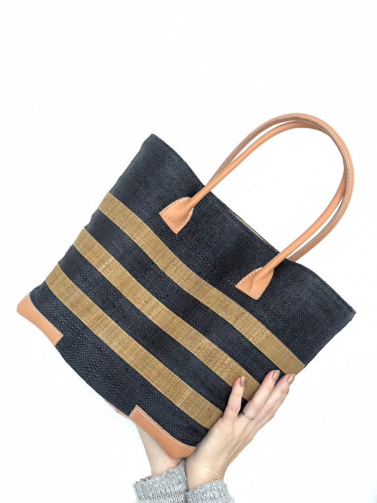 Model wearing Jacky Black Small Straw Basket Bag handmade loomed raffia palm fiber in black with three centered horizontal stripes of tobacco/cinnamon/brown handbag purse with leather handles and detailing - Shebobo