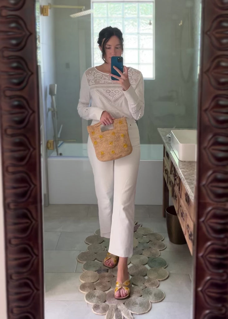 Model wearing Daisy Crochet Straw & Leather Sandal with Flower Embroidery & Metallic Detailing handmade crochet natural raffia palm fiber in a solid hue of natural straw color in two bands with saffron yellow petals and coral orange/red centered embroidered flower pattern wrap around the top  of the shoe with a band of metallic gold across the top summer sandals shoes - Shebobo (with Mini Concon Flower Embroidery Straw Basket Purse)