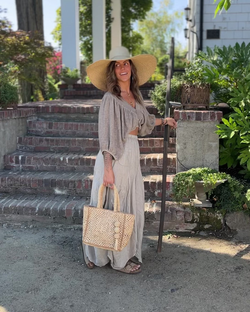 Model wearing Kimba Crochet Handbag with Sphere Tassel Charm Embellishment handmade natural raffia palm fibers crochet into a granny square pattern with cappuccino/light brown detail edging - Shebobo (with Natasha 7" Wide Brim Woven XL Straw Sun Hats)