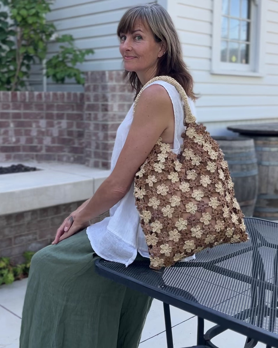 Model wearing Amalie Two Tone Daisy Flower Crochet Straw Handbag handmade crochet mini flower buds from crochet natural raffia palm fiber in an alternating colored pattern of cappuccino tea/light/brown and natural straw color with brown internal liner and natural woven handles purse - Shebobo