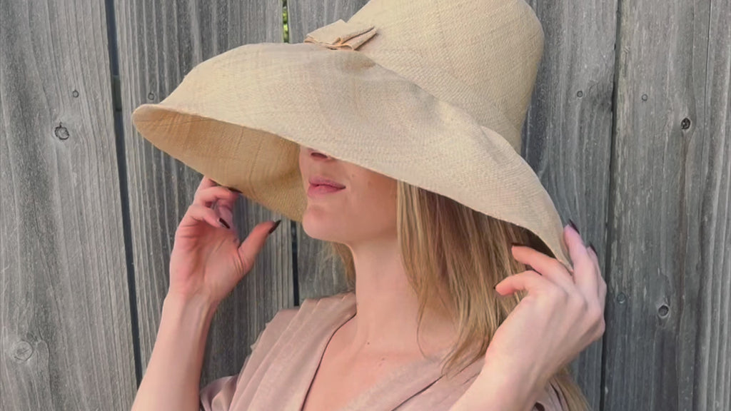 Model wearing 7 inch wide brim packable straw sun hat in natural - handmade loomed raffia palm fiber in a solid hue of natural straw color can be worn may ways to suit your style - Shebobo